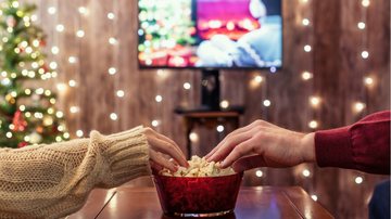 Duas pessoas comendo pipoca e assistindo filmes de Natal românticos - FTiare/iStock