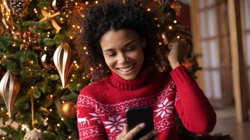 Jovem adulta enviando mensagens de Natal para os amigos - fizkes/iStock