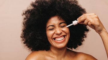 Mulher negra de cabelos cacheados passando cosmético no rosto - JLco - Julia Amaral/iStock