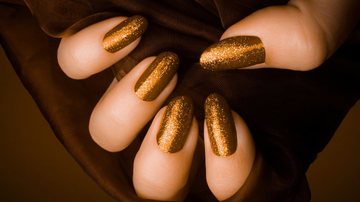 As unhas douradas dão um quê de elegância para qualquer look. - baiajaku/ iStock