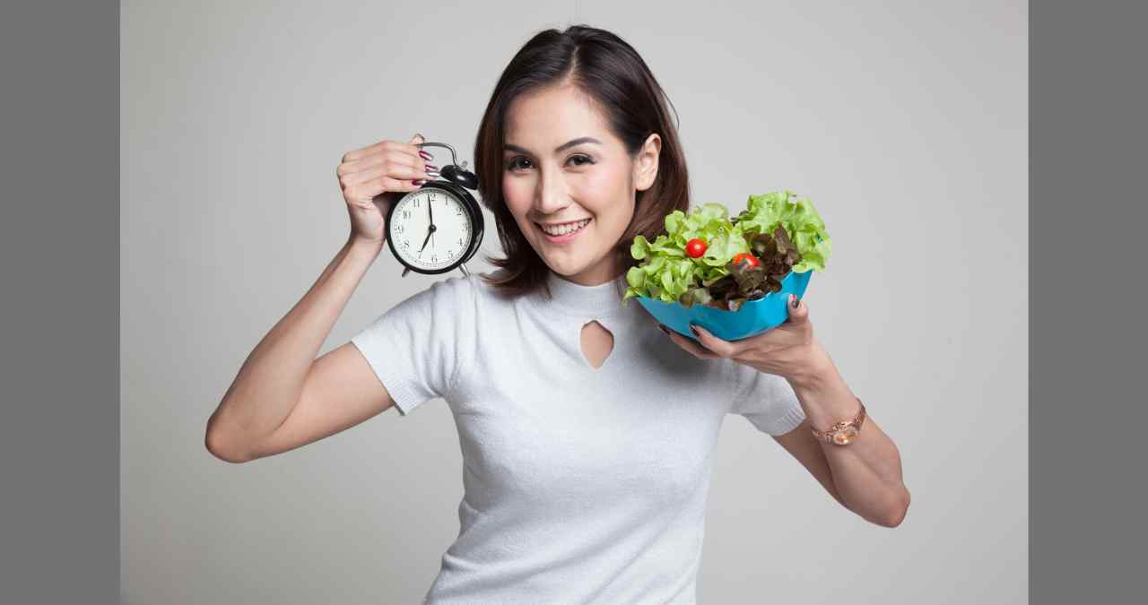 mulher posando com um relógio na mão direita e uma salada na mão esquerda