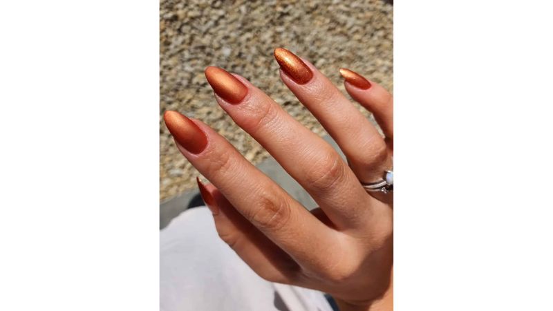 As unhas metalizadas são uma das principais nail arts de 2023, vale a pena combiná-la com o esmalte laranja, resultando em um tom cobre.