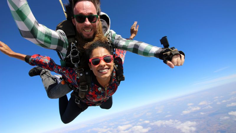 homem e mulher pulando de paraquedas e sorrindo para a câmera