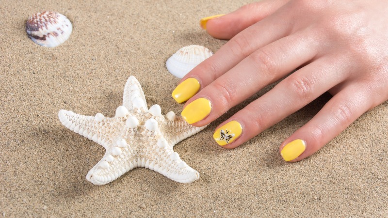 Unha amarela na praia com adesivo