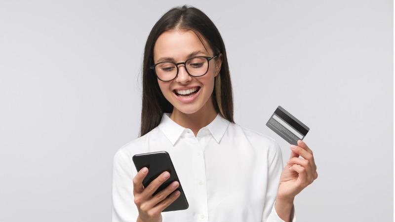 jovem mulher sorrindo e segurando cartao de credito e celular