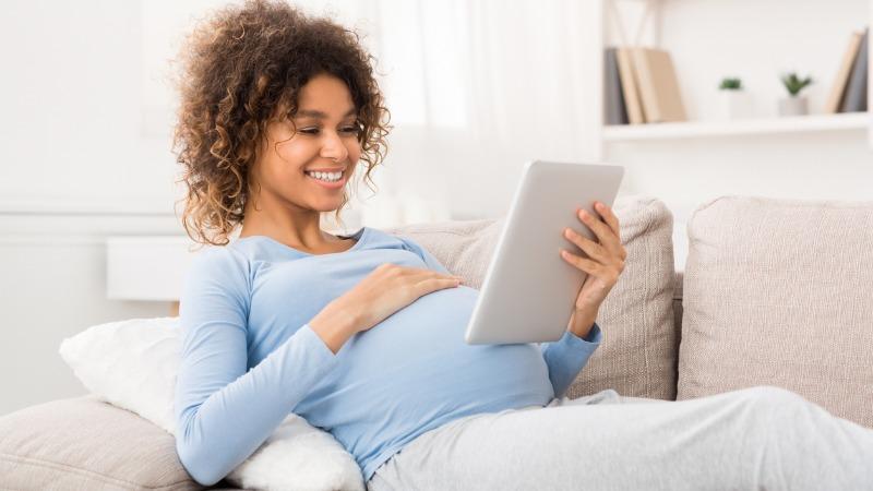mulher gravida rindo e usando um tablet