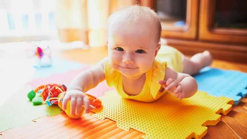 Bebê feliz em um tapete emborrachado para ilustrar Tapete para quarto de bebê: 7 dicas para escolher o ideal