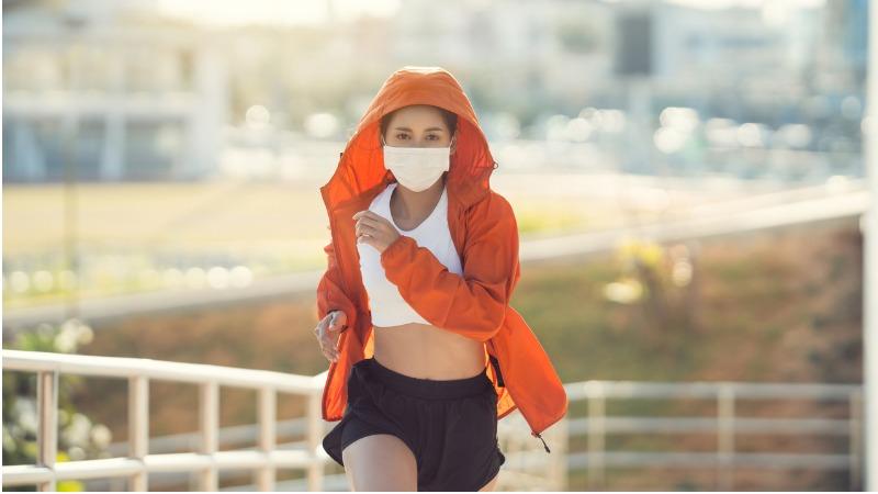mulher se exercitando ao ar livre com mascara de protecao