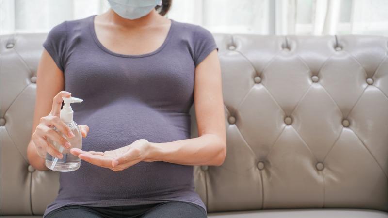 mulher gravida de mascara passa alcool gel nas maos