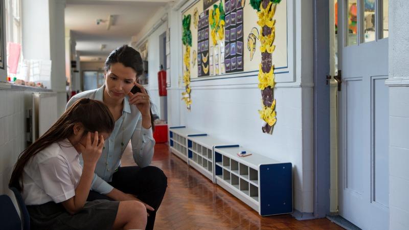 menina triste na escola sendo consolada por professora